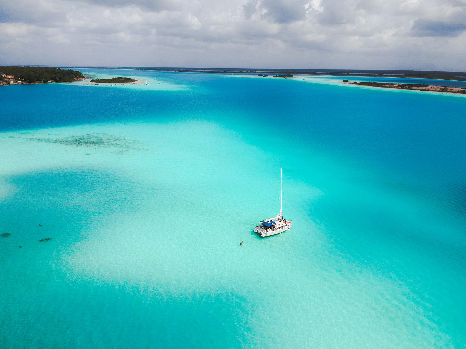 A catamaran anchored on a vivid turquoise shelf of the Laguna de los Siete Colores, seen from above