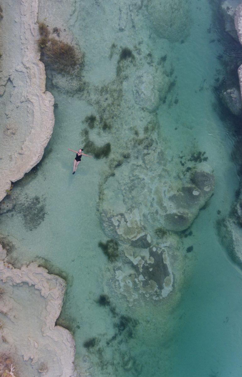 A swimmer floating in the clear shallows above pale limestone formations