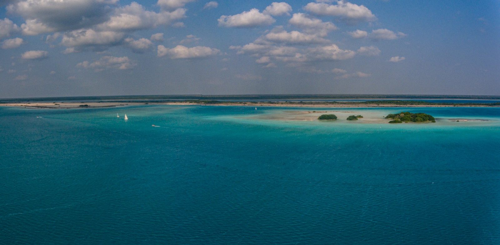 Open turquoise water dotted with small mangrove islands and a distant sailboat
