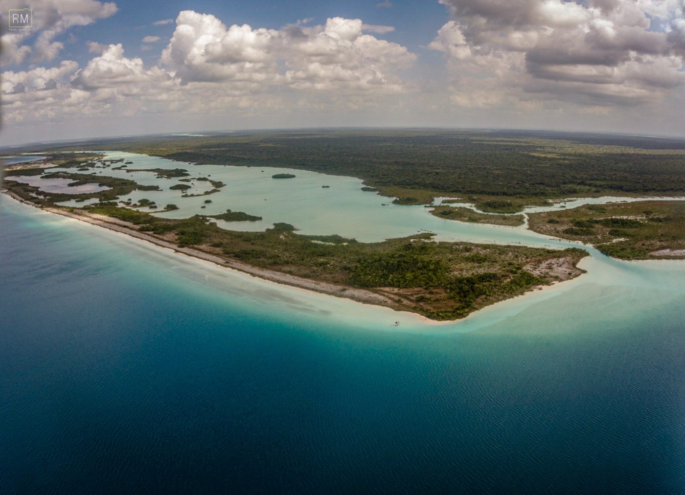 A wide aerial of the lagoon's sandy peninsula reaching into bands of turquoise