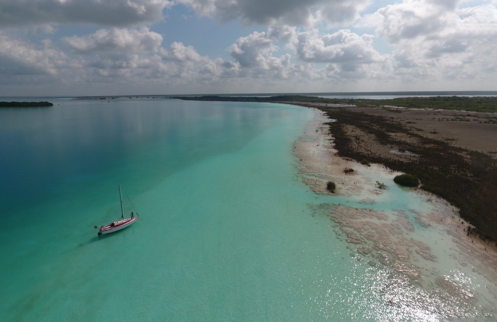 A sailboat anchored in shallow turquoise water along a sandbar