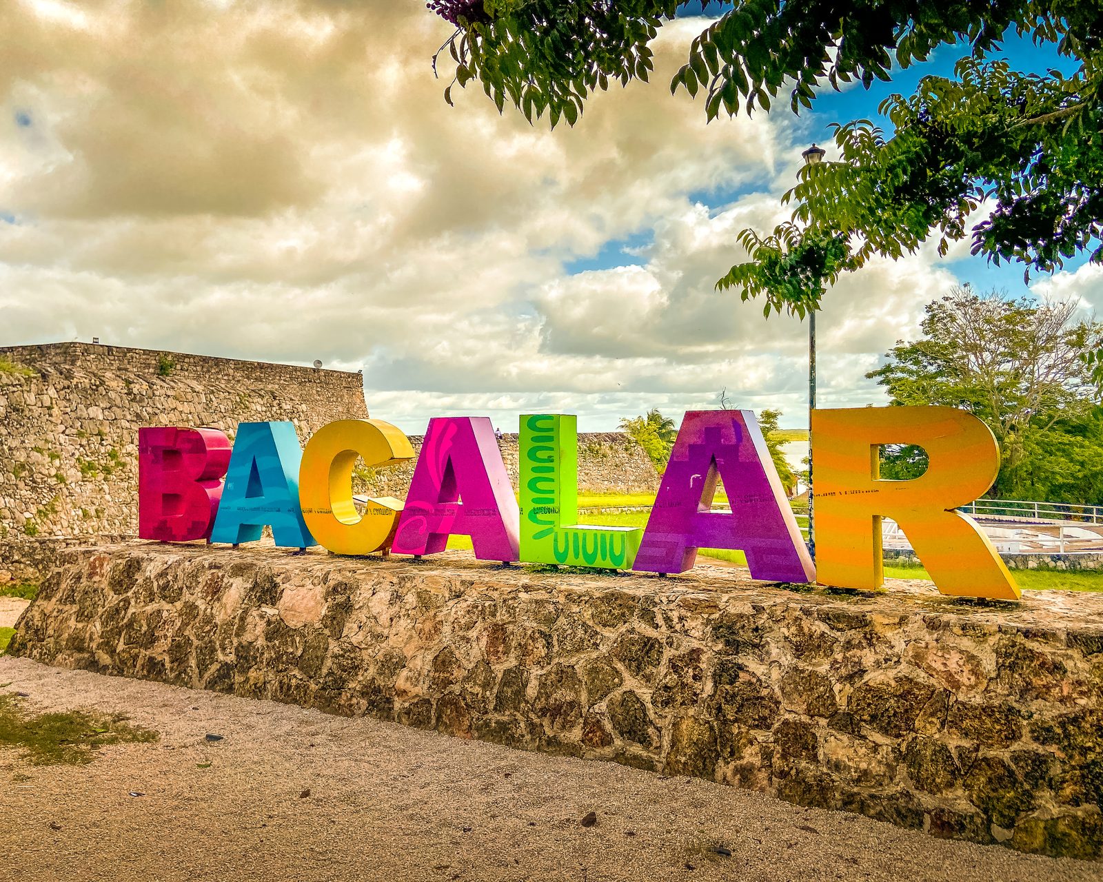 The brightly colored BACALAR letters on a stone wall beneath a dramatic cloudy sky