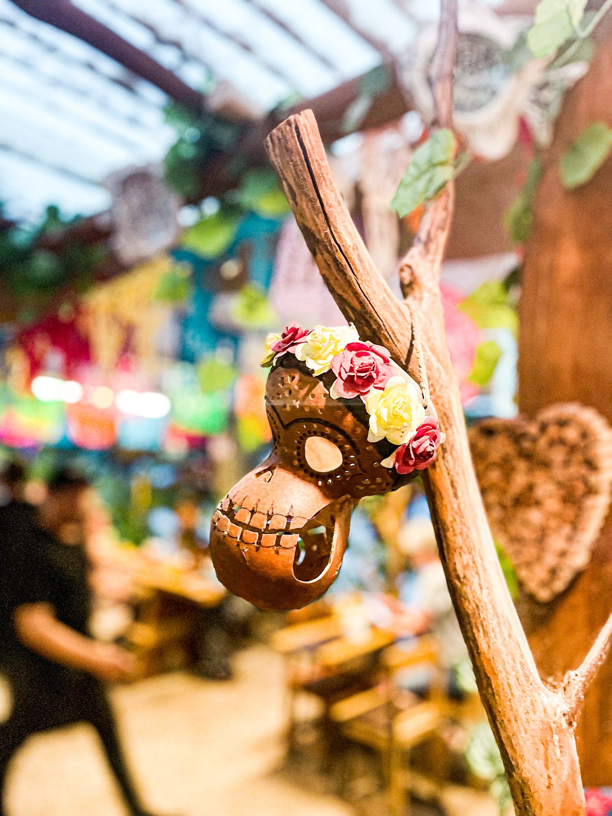 A hand-painted clay calavera crowned with paper roses hanging in a festive courtyard